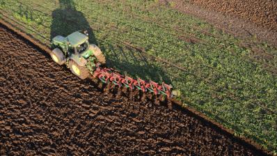 Tracteur vert en train de labourer un champ. 